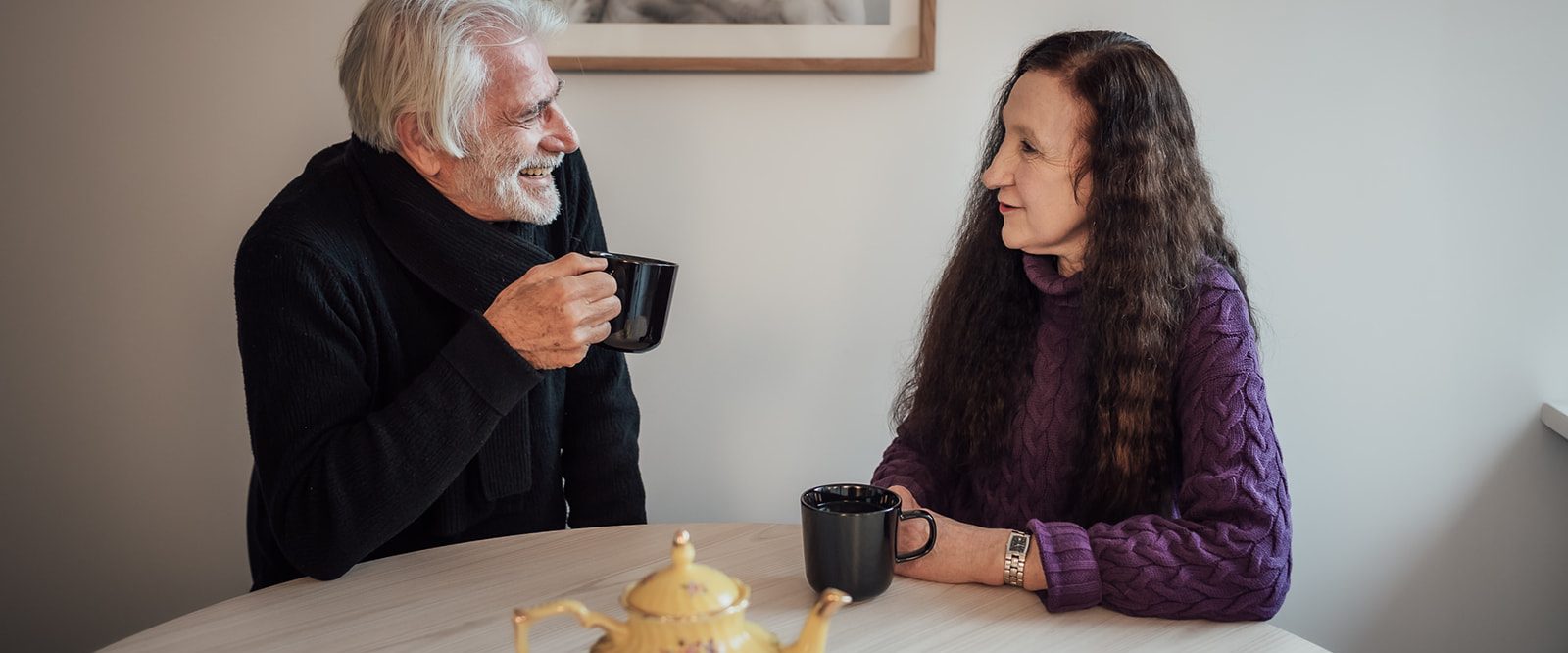 A man and woman laughing, seated at a table drinking tea.