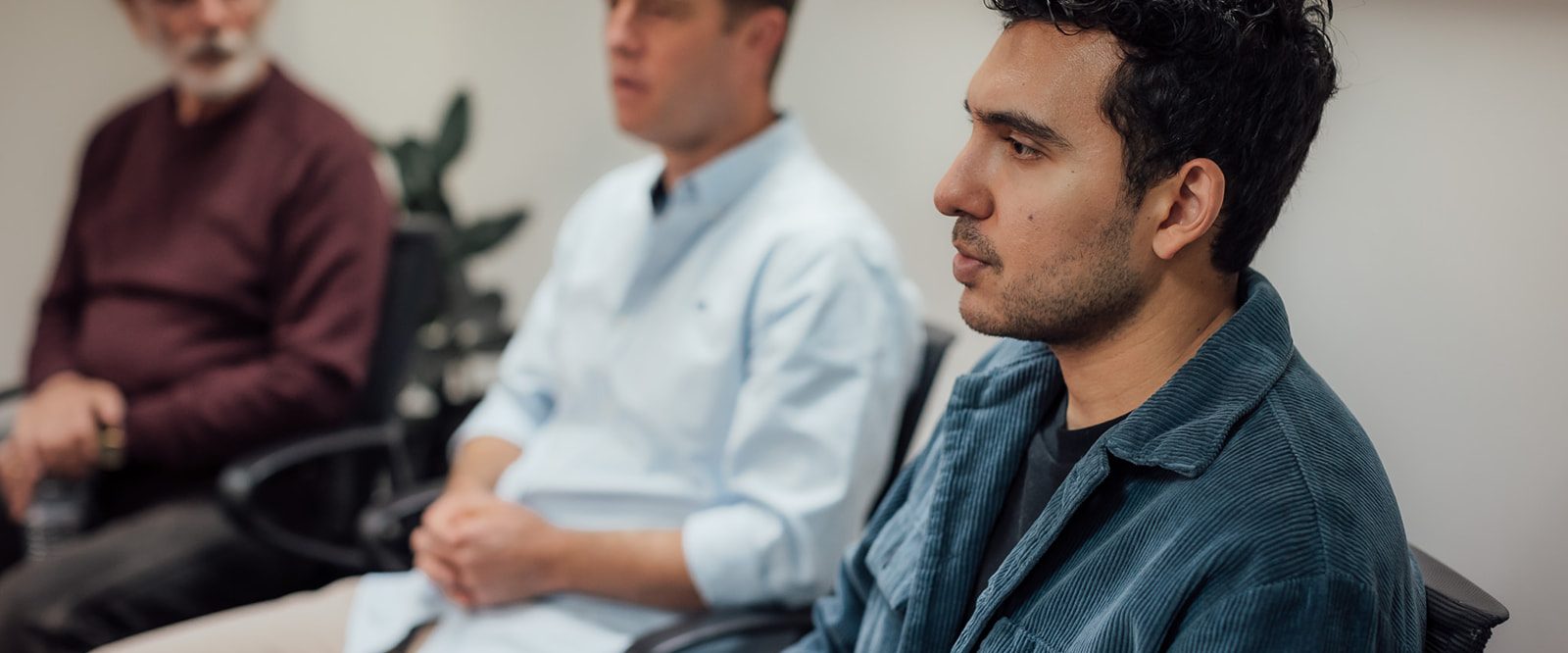 Three men sitting on chairs listening to someone talking.