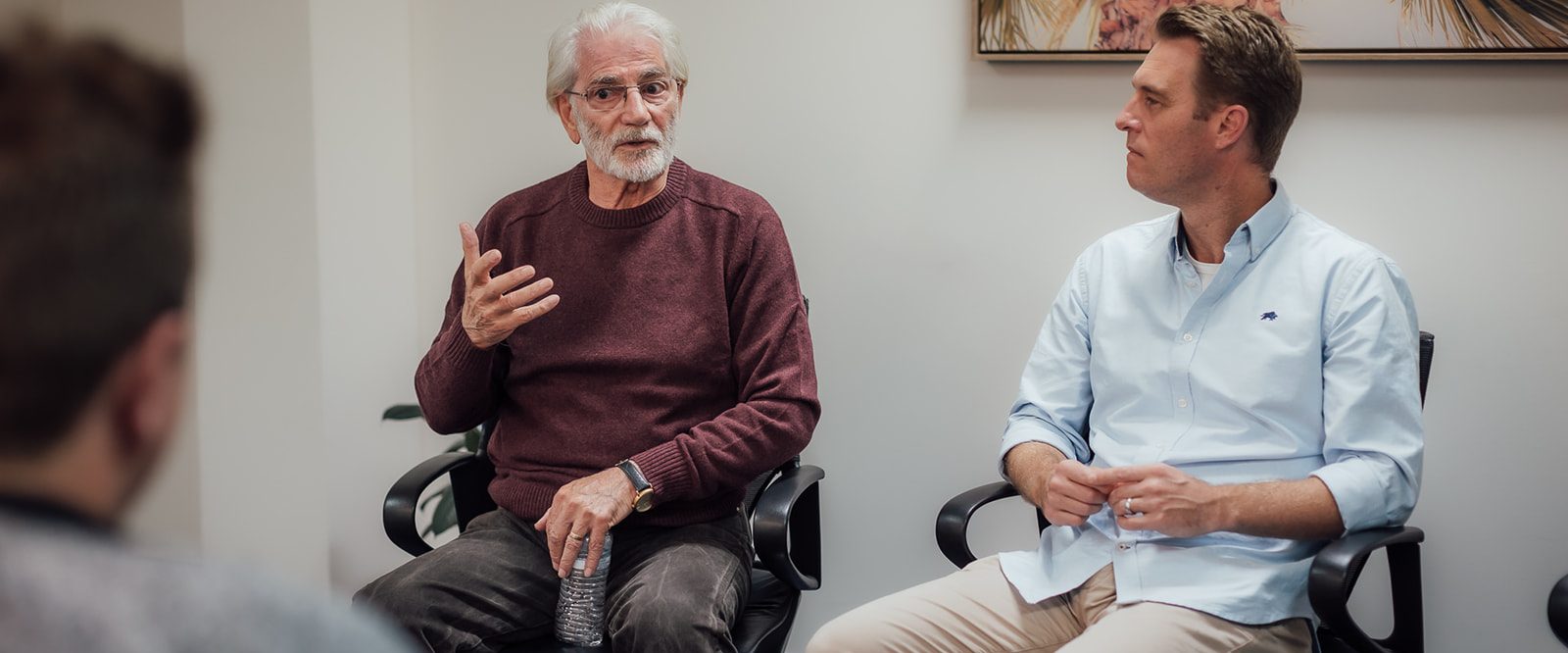 A man talking in a room with two men, sitting in a group.